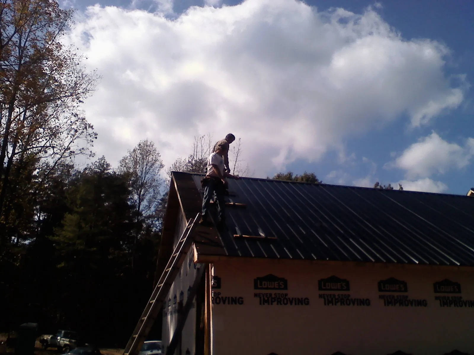 Roofer fastening dark metal panels high against a cloudy sky, from a Roof Inspection job in Mercer