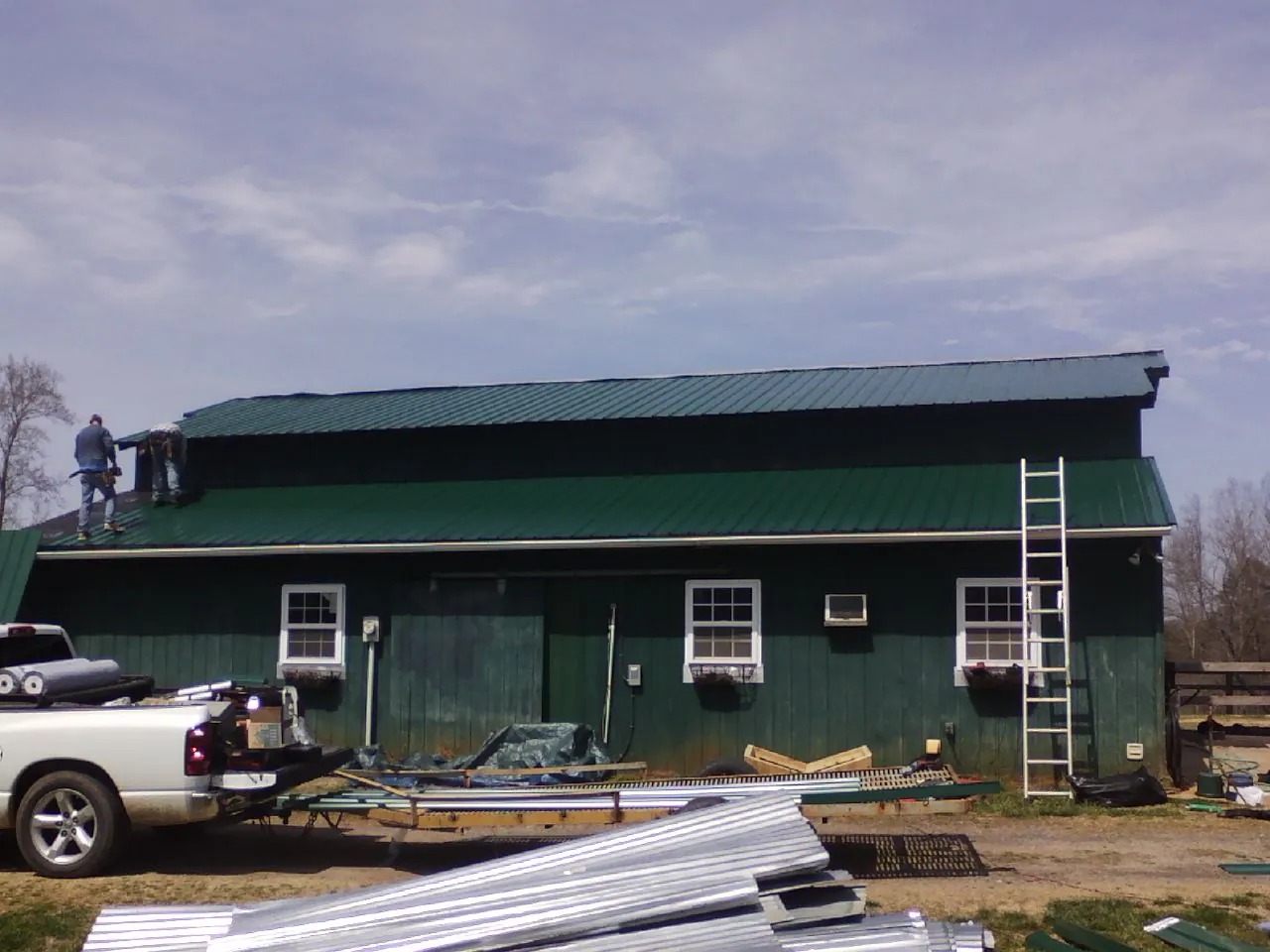 Crew installing green metal roofing on a large green barn in Mercer
